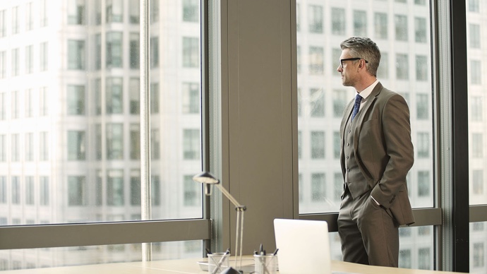Businessman wearing glasses and suit looking out of office window in city