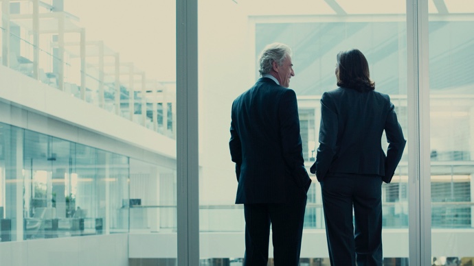 Two well-dressed corporate people talking near glass wall in modern office